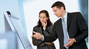 Businessman and Businesswoman discussing in front of a flip-chart.